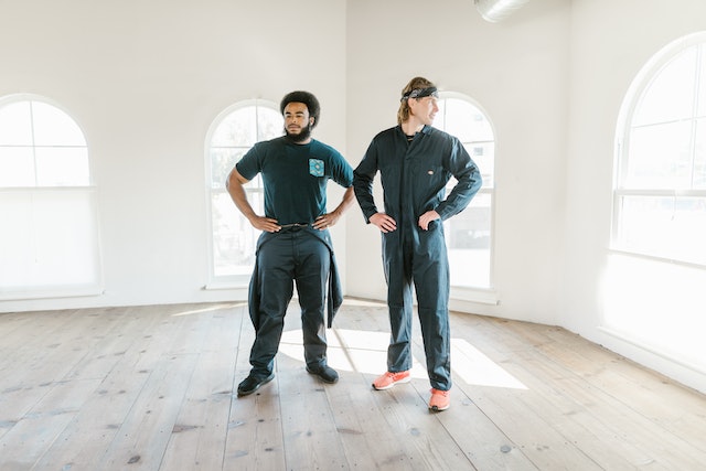 two people wearing dark jumpsuits standing in an empty home with hands on hips