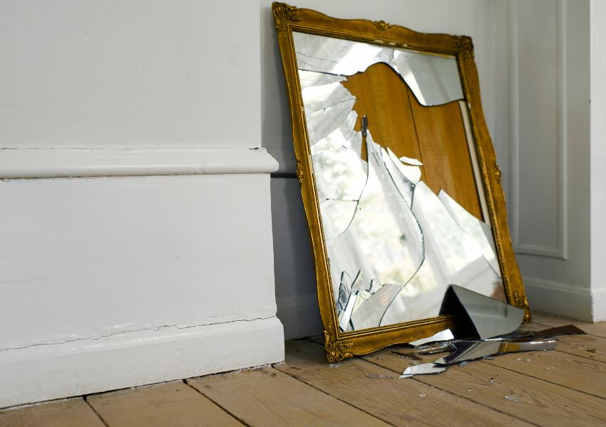A shattered wooden mirror sits on the floor of a rental unit, damaged by a tenant.