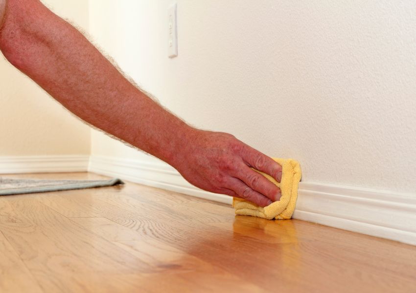 A tenant's arm is in frame as they wipe the baseboards of their rental unit with a yellow cloth.