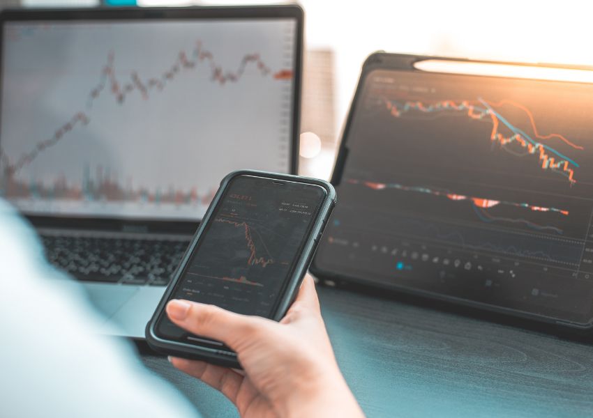 An investor monitors the stock market on their phone, tablet and laptop as some of their investments depreciate in value.